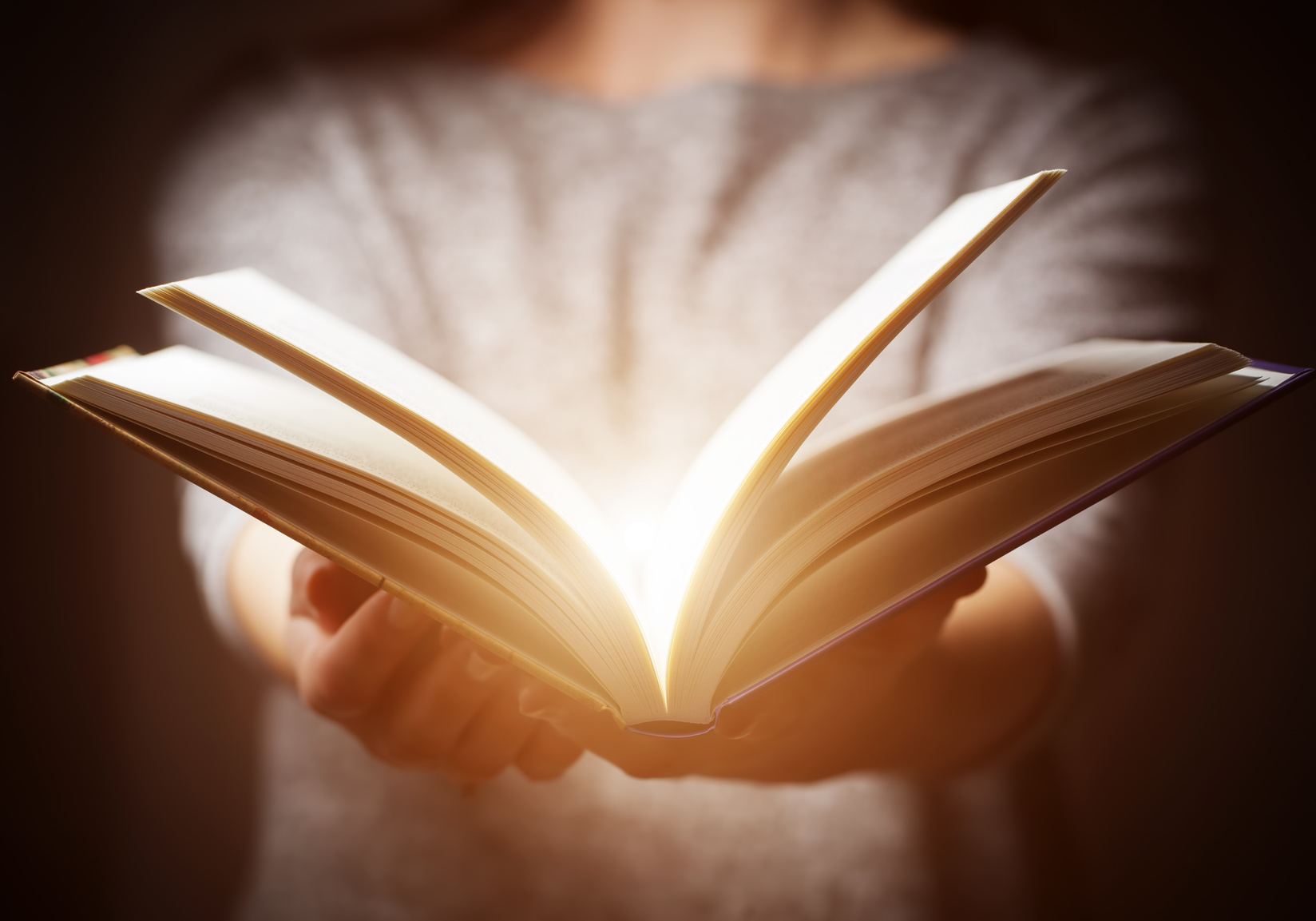 Light coming from book in woman’s hands in gesture of giving