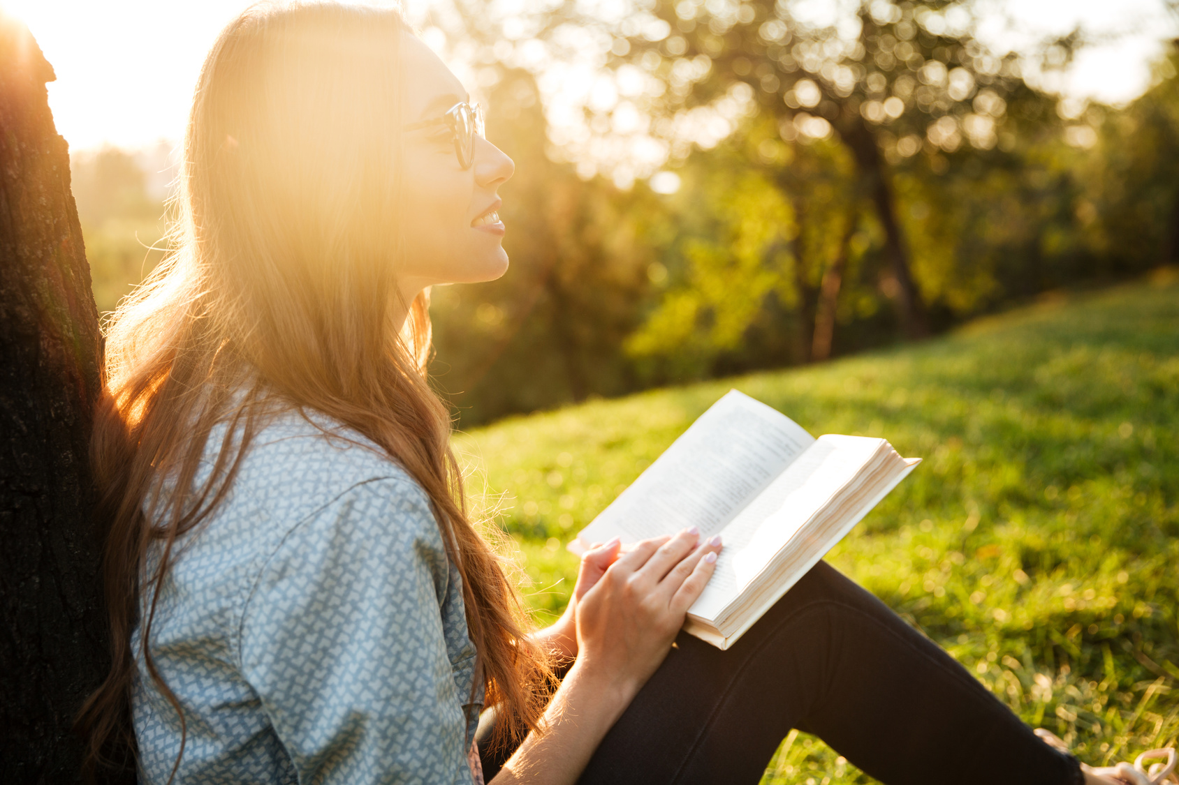Side view of pretty brunette woman sitting near the tree