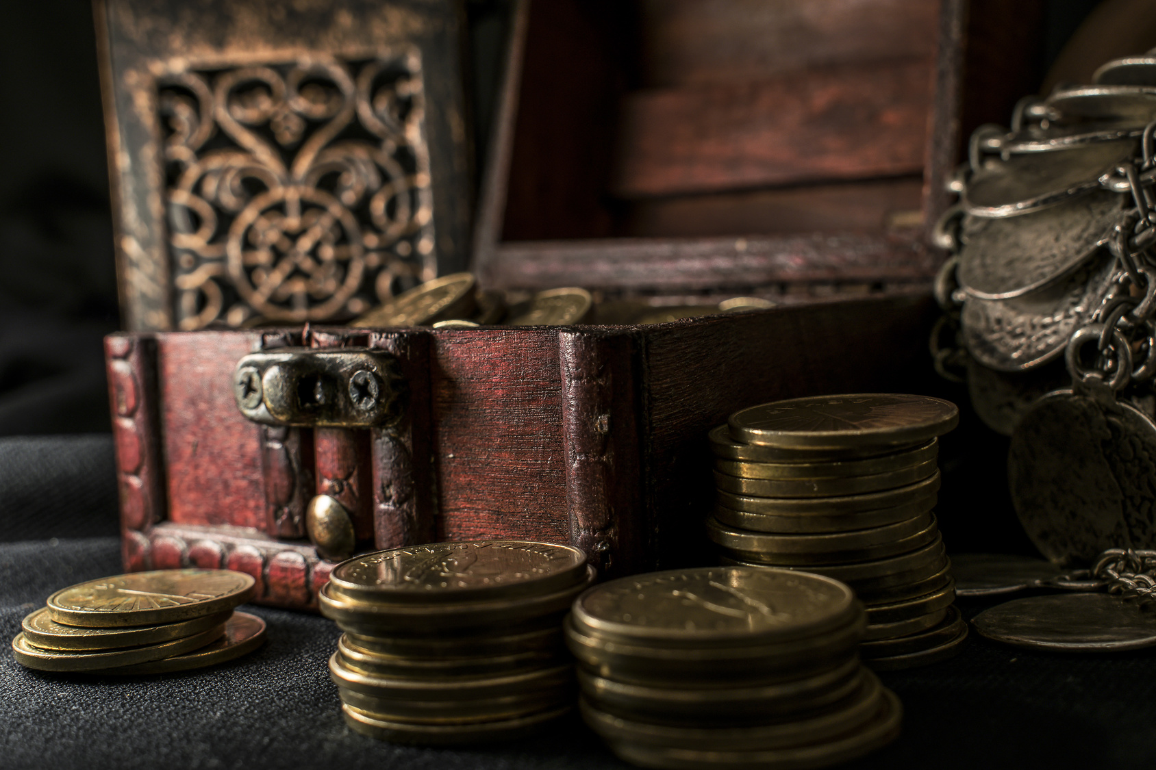 Treasure chest, pile and pillar of coins, a ceramic bowl filled with jewelry coins and candle lamp in dark environment