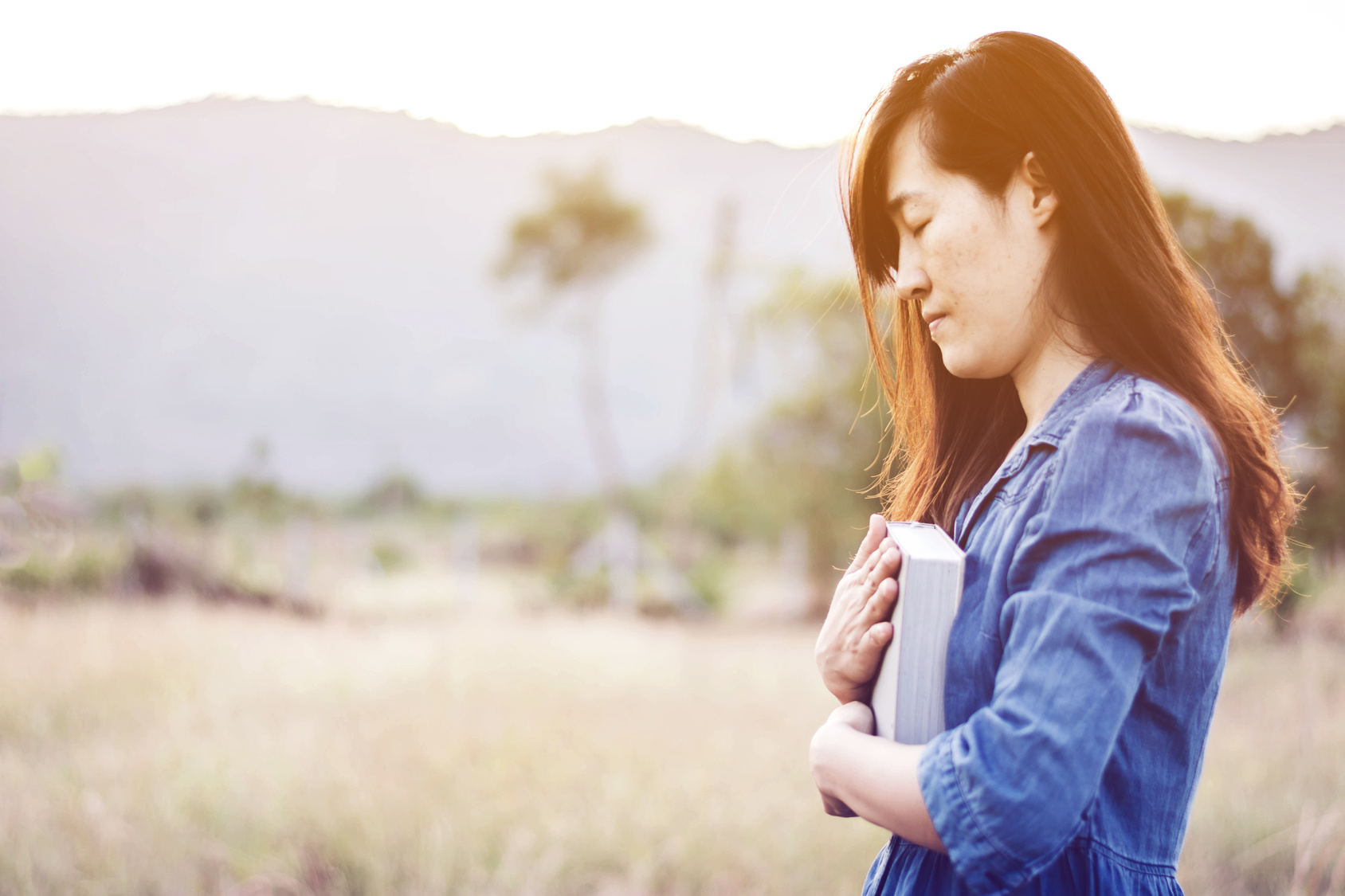 Woman praying in meadow at sunset
