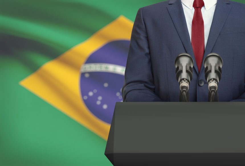 Businessman or politician making speech from behind a pulpit with national flag on background &#8211; Brazil