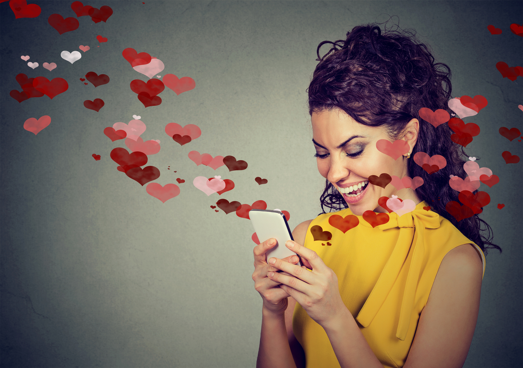 Beautiful happy woman sending love text message on mobile phone with red hearts