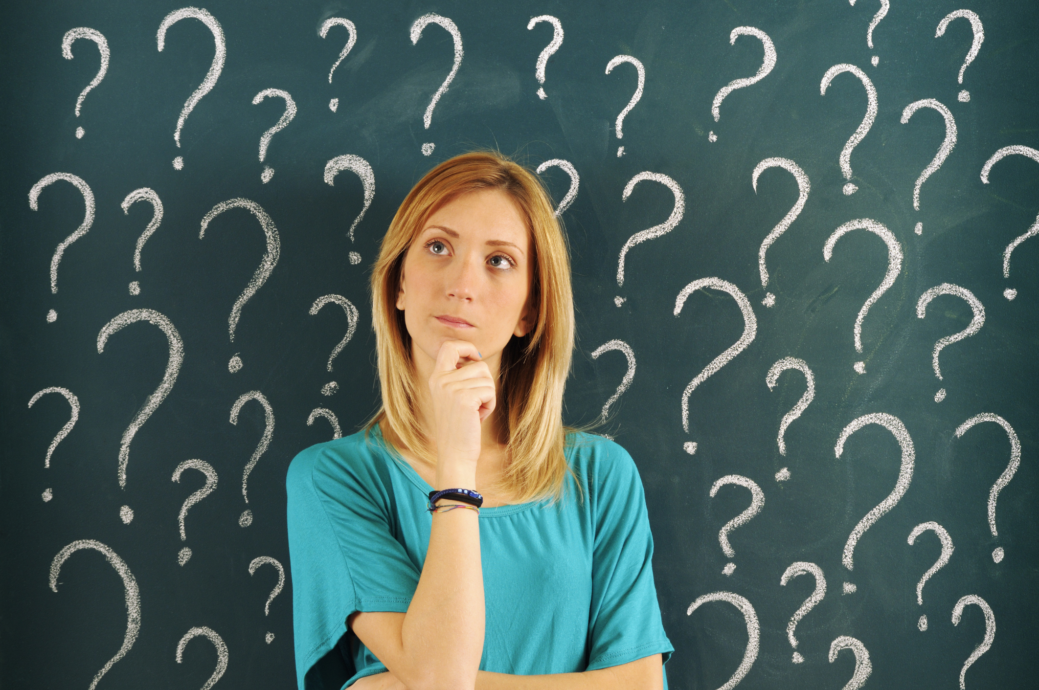 Pensive Woman in front of Question Marks Sketched on Blackboard