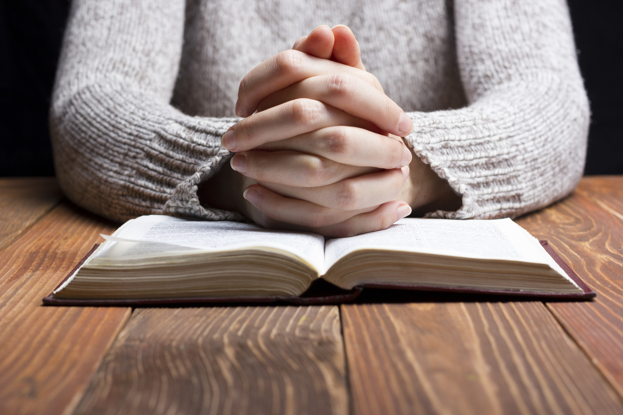 Woman hands praying with a bible in dark over wooden