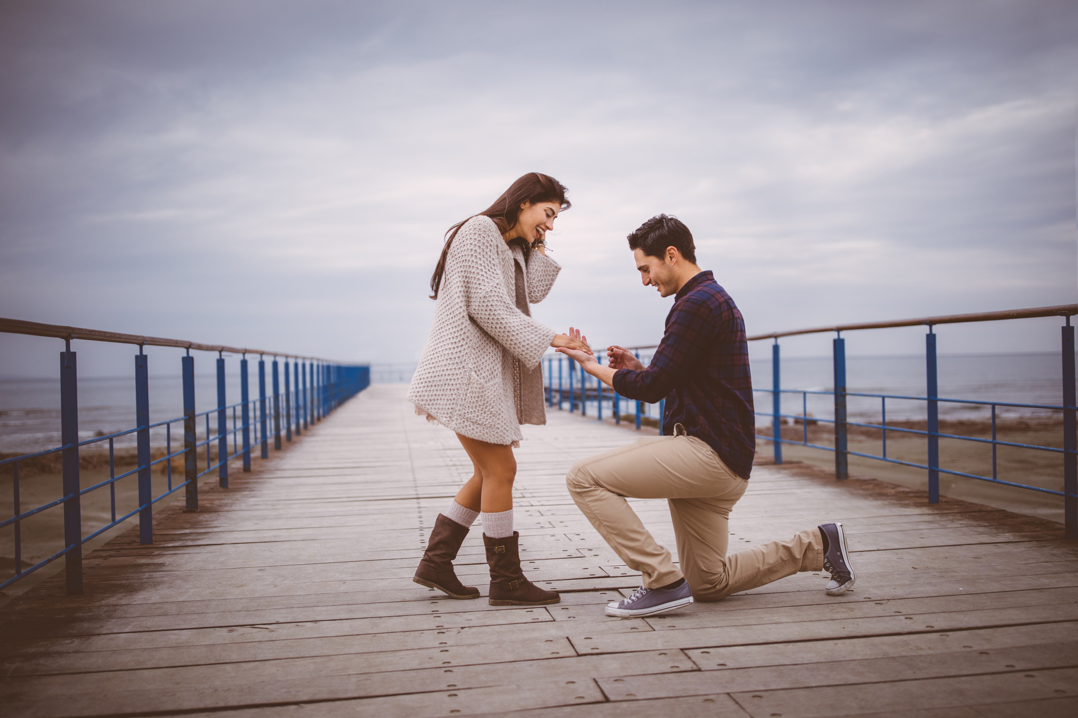 Man on one knee proposing to girlfriend on a pier