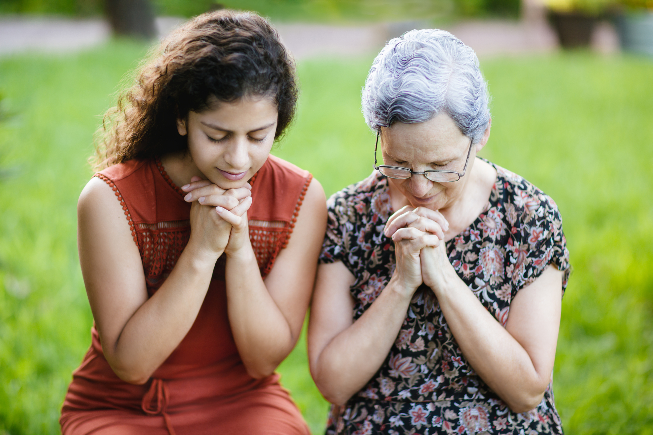 Young woman and grandmother praying with hands together