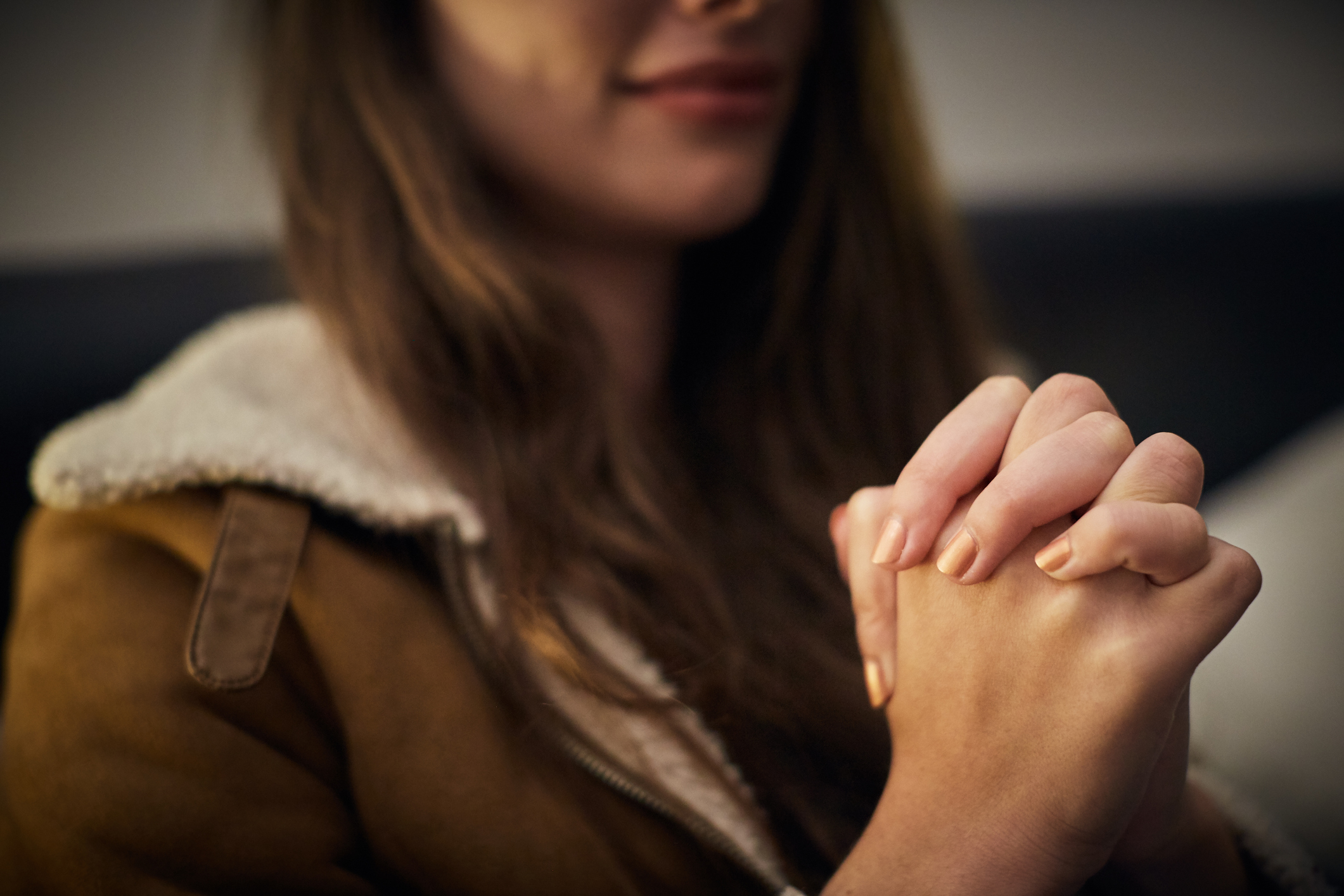 Gently smiling young woman prays, hands clasped