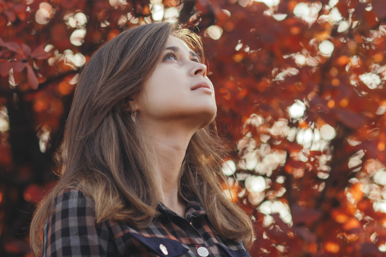 profile of a beautiful young woman looking up gratefully, girl walking through autumn nature in a park