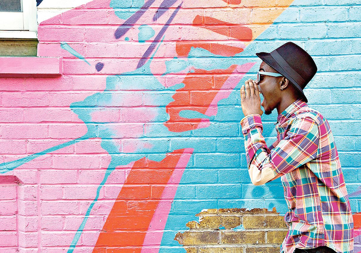 Black man in sunglasses shouting near colorful wall