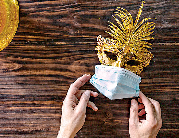 Golden glitter hat, golden mask and face mask protective on dark wooden table. Human hands adjust the face mask protective