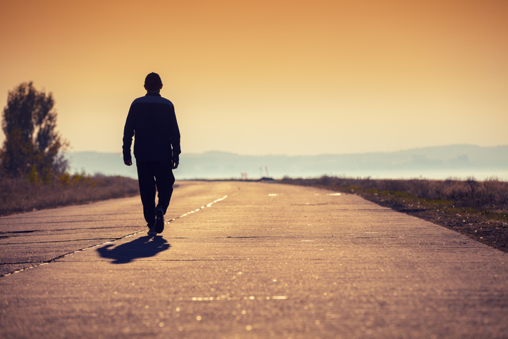 A man walks along a concrete road along the sea at a golden sunset and looks at the mountain