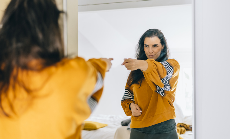 Self confident single woman pointing finger at her reflection in mirror, dancing and felling good