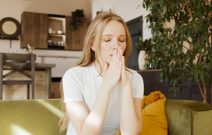 Young worried woman sit home with closed eyes put hands in prayer