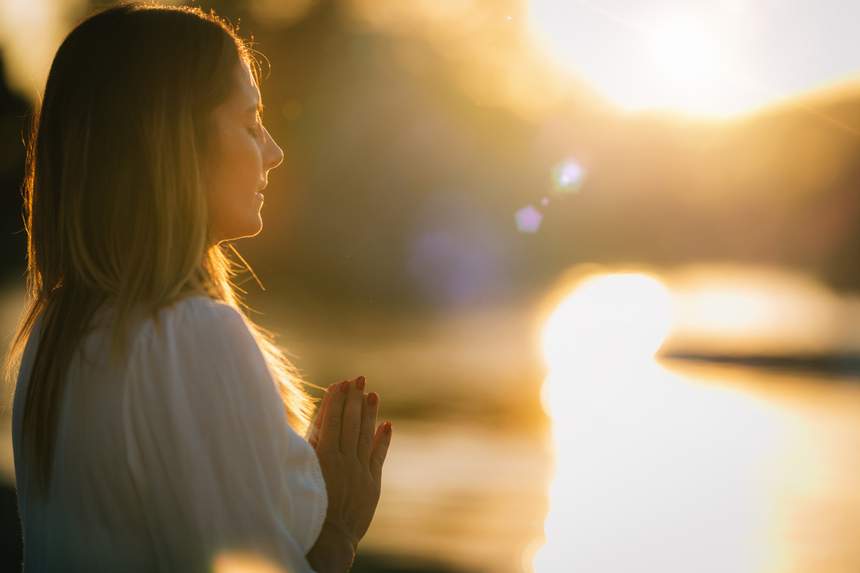 Sunset Meditation. Woman Meditating by the Lake in Prayer Position.