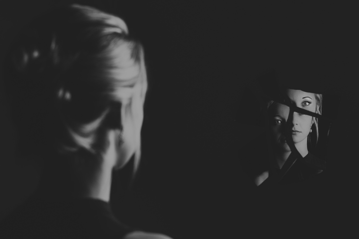 Woman looking at her face in shards of broken mirror pieces artistic conversion