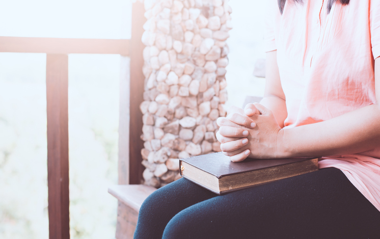 Woman hands folded in prayer on a Holy Bible  for faith concept in vintage color tone