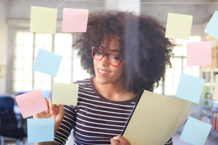 Smiling young woman looking at window with sticky notes