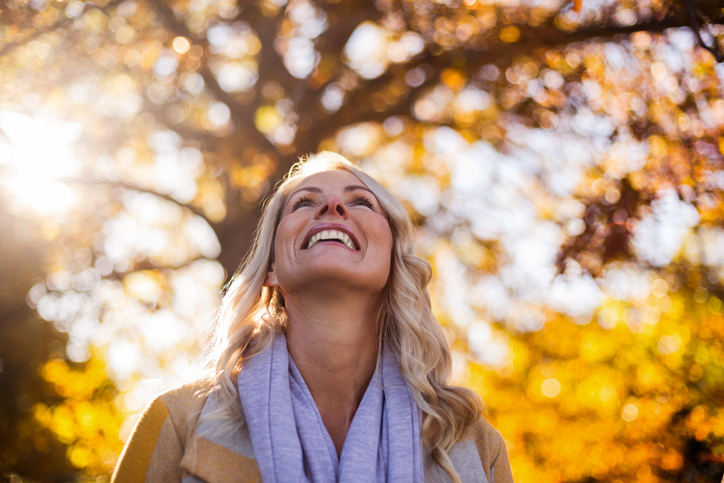 Smiling woman looking up against trees