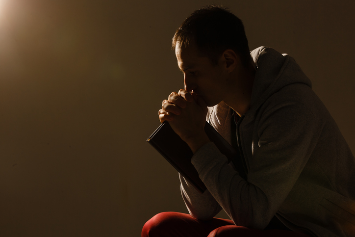 Religious young man praying to God on dark background, black and white effect