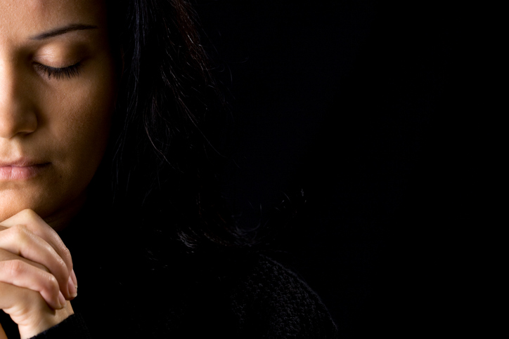 A woman deep in prayer and a black background