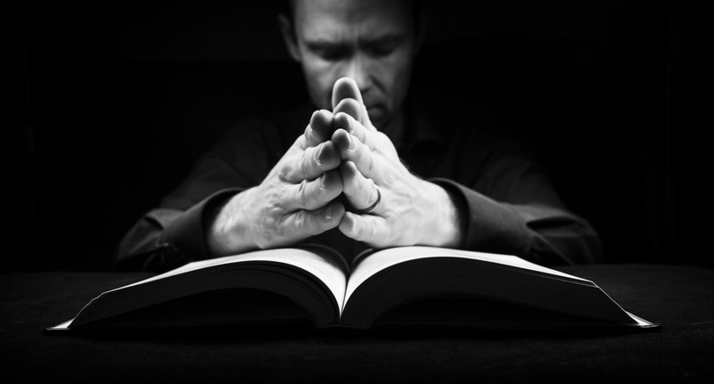 Man praying to God with his hands resting on a bible