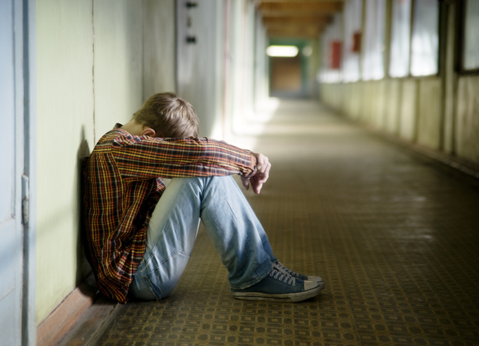 Teenager sitting on empty hallway with head buried in arms