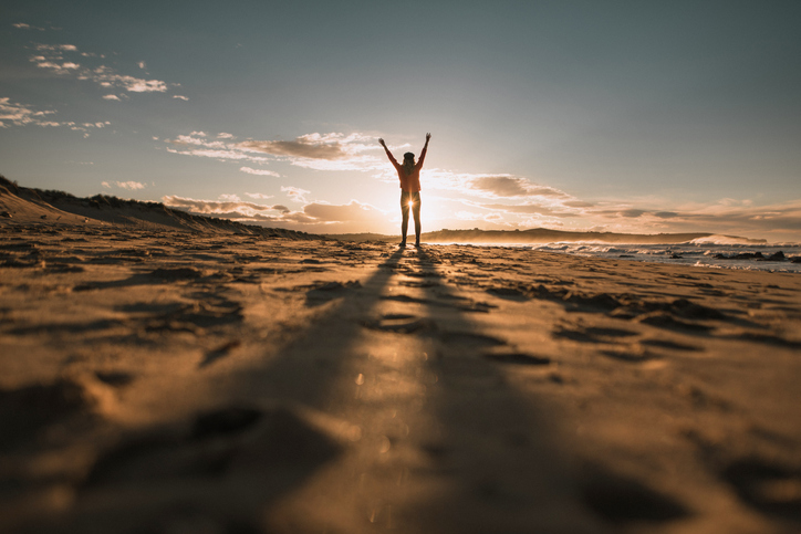 Young woman with arms raised at sunset