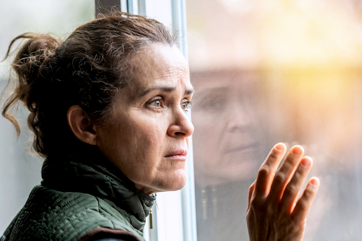 Concerned, pensive, unemployed mature woman looking through a window