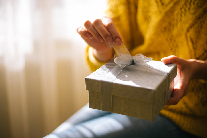 Young woman in yellow sweater opening gift box