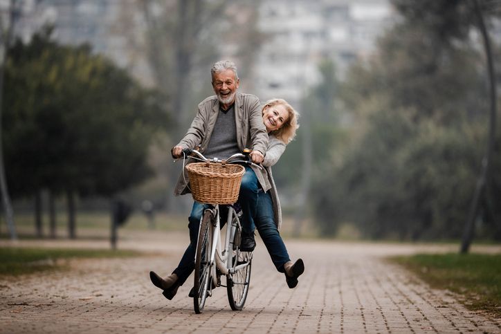 Playful senior couple having fun on a bike in autumn day.