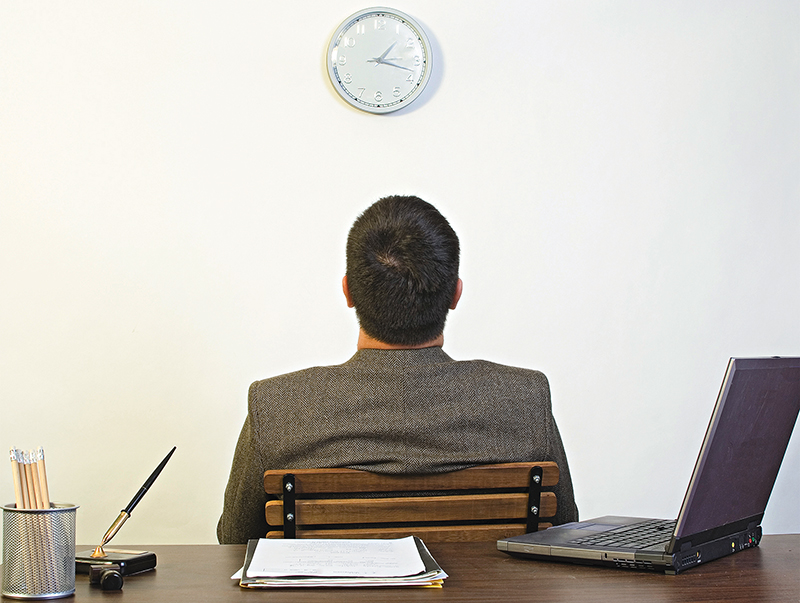 A man sitting backing against a desk looking up at a clock