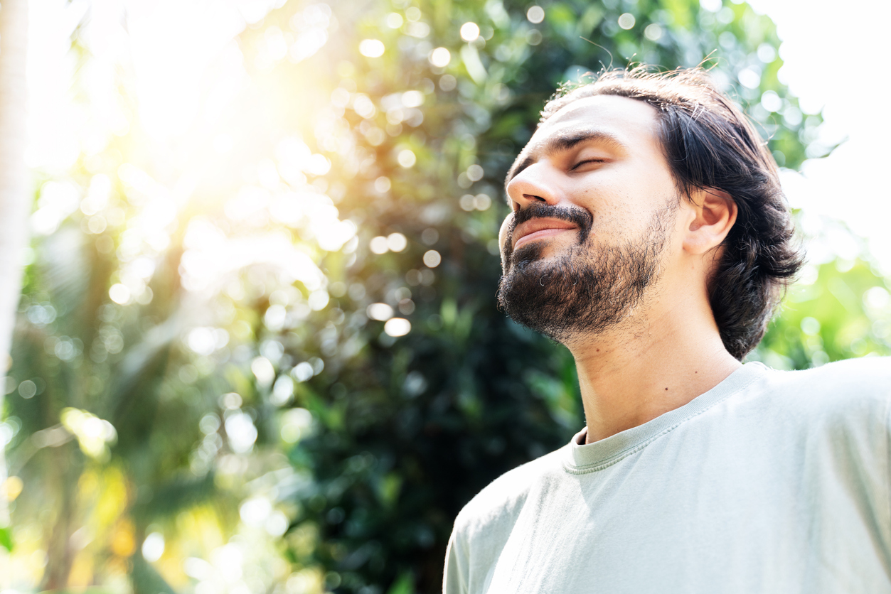 A bearded man is meditating outdoor in the park with face raised up to sky and eyes closed on sunny summer day. Concept of meditation, dreaming, wellbeing healthy lifestyle