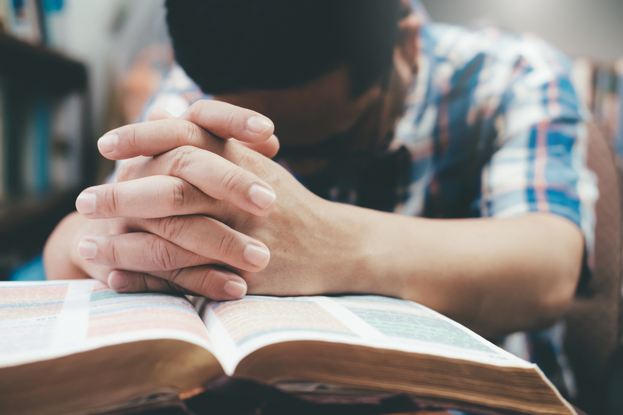 Man praying, hands clasped together on her Bible.