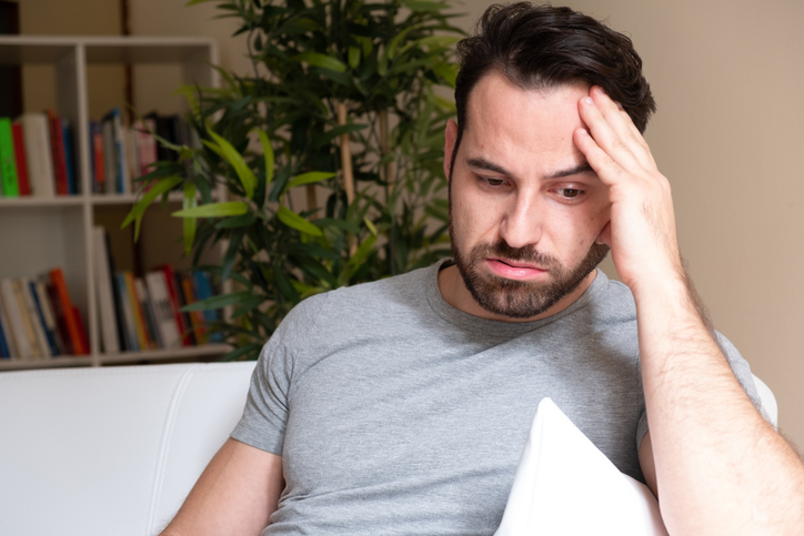 Man suffering and feeling alone at home sitting on the sofa
