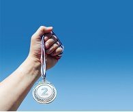 A hand holds up a second-place silver medal, with the sky in the background. Victory concept