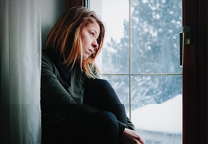 Sad woman sitting by the window looking outside