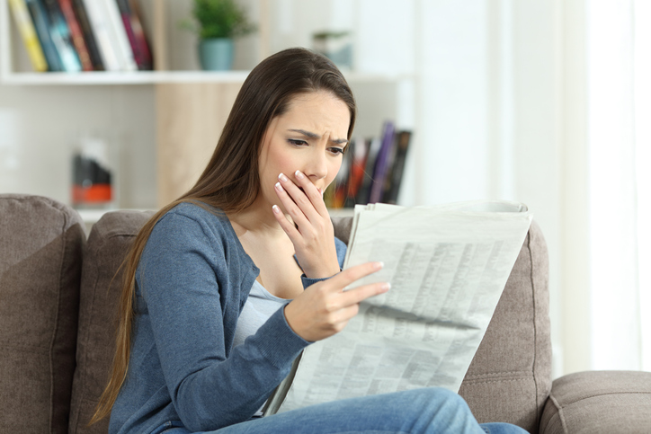 Worried woman reading bad news in a newspaper at home