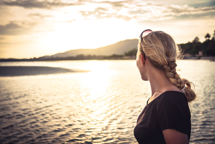 Lonely young woman tourist looking into the sea horizon during beautiful sunset during summer beach holidays