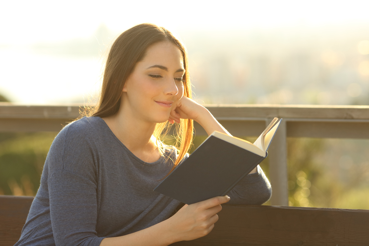 Woman reading a hard cover book at sunset on a park