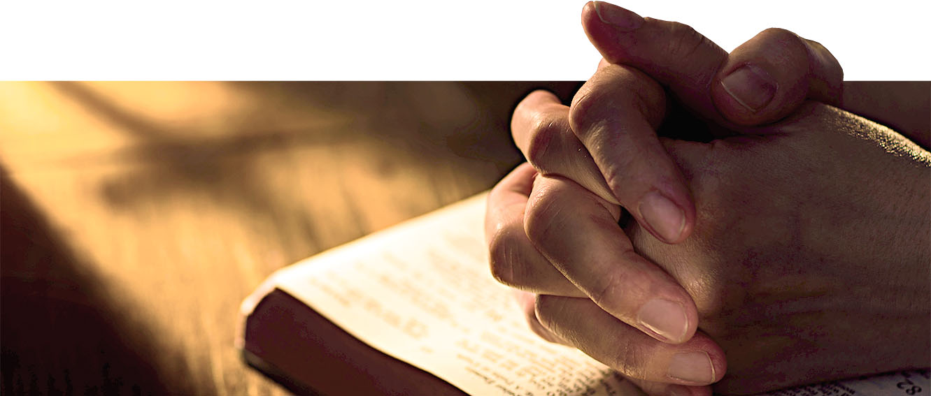 Close up of hands clasped on open Bible