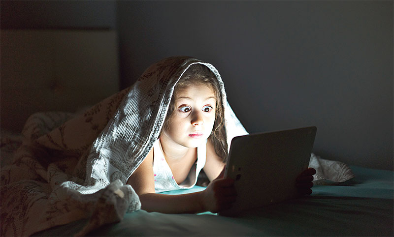 Little girl using digital tablet in her bed at night