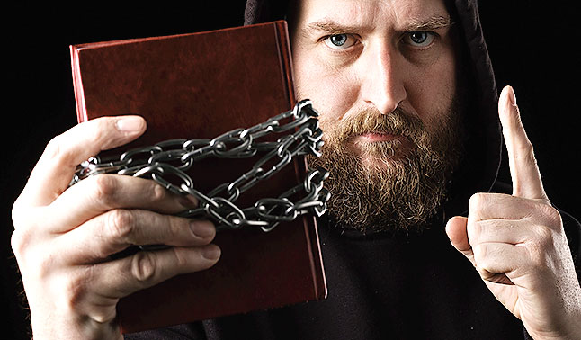 a white bearded man calls for attention, holds a book in his hand, it is tied with a chain