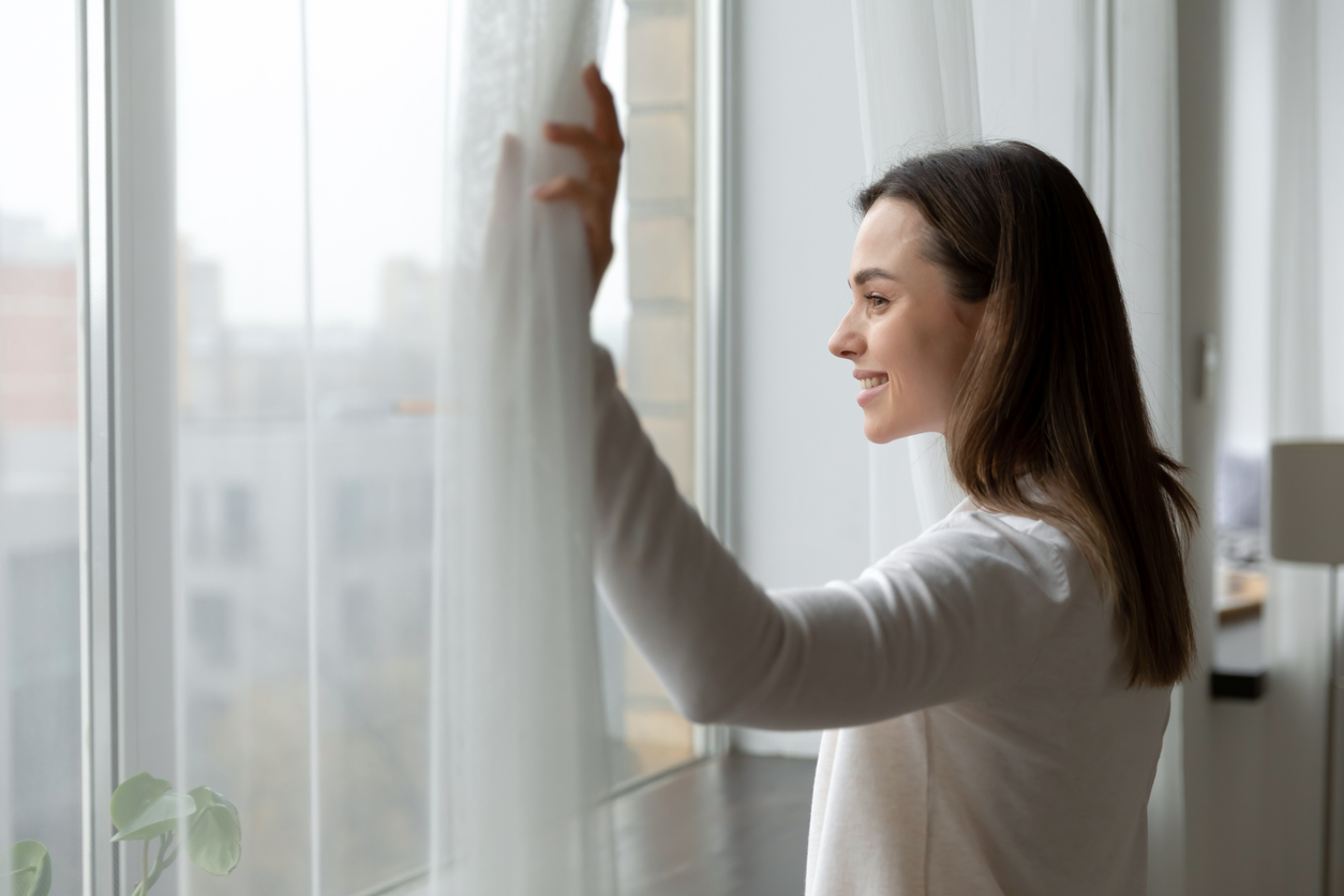 Side view happy attractive woman opening curtains.