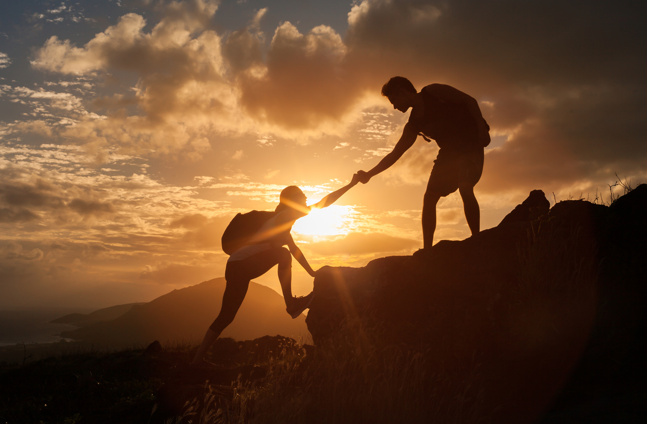 Male and female hikers climbing up mountain cliff and one of them giving helping hand.