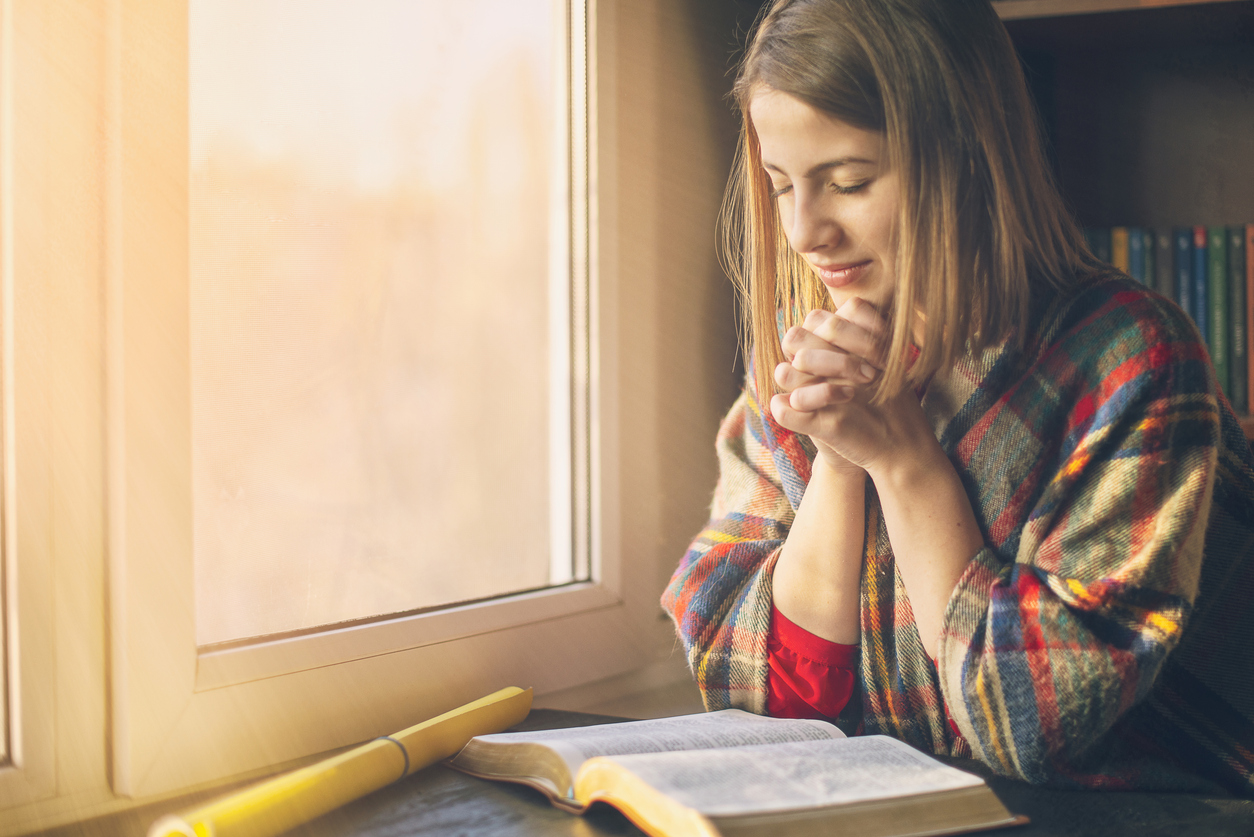 Beautiful woman praying having the Bible opened in front of he