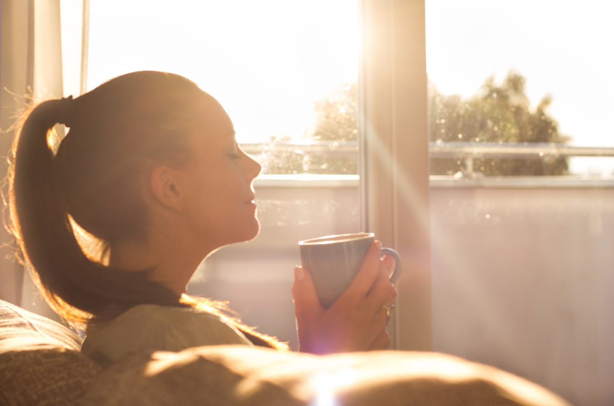 Girl smelling coffee beside window in the morning