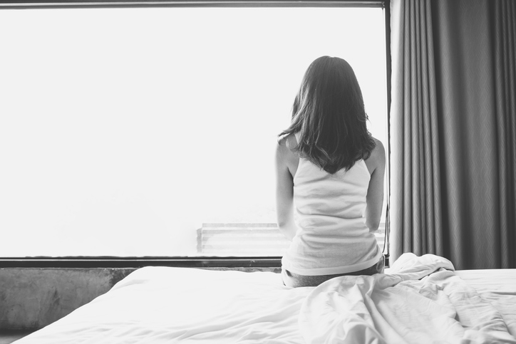 Portrait of depressed woman sitting alone on bed in bedroom.