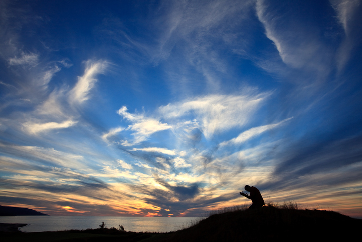 Silhouette of Man On His Knees In Prayer By The Ocean Against Beautiful Sunset Sky