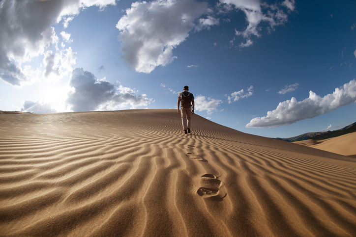 Lonely man walks in desert dunes