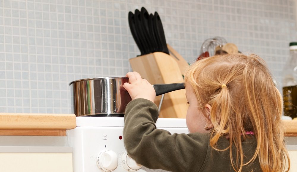 Stove danger in kitchen for a small child with blond hair
